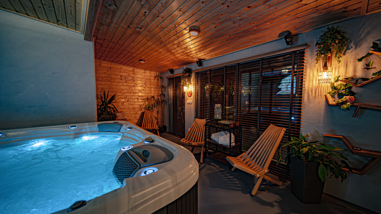 Agroturystyka Za Piecem – Przytulny wewnętrzny pokój spa z podświetlaną wanną z hydromasażem, drewnianym sufitem, rozkładanymi fotelami, roślinami doniczkowymi i ciepłym oświetleniem - idealny na wypoczynek na wsi i noclegi dla rodzin z dziećmi szukających relaksu.